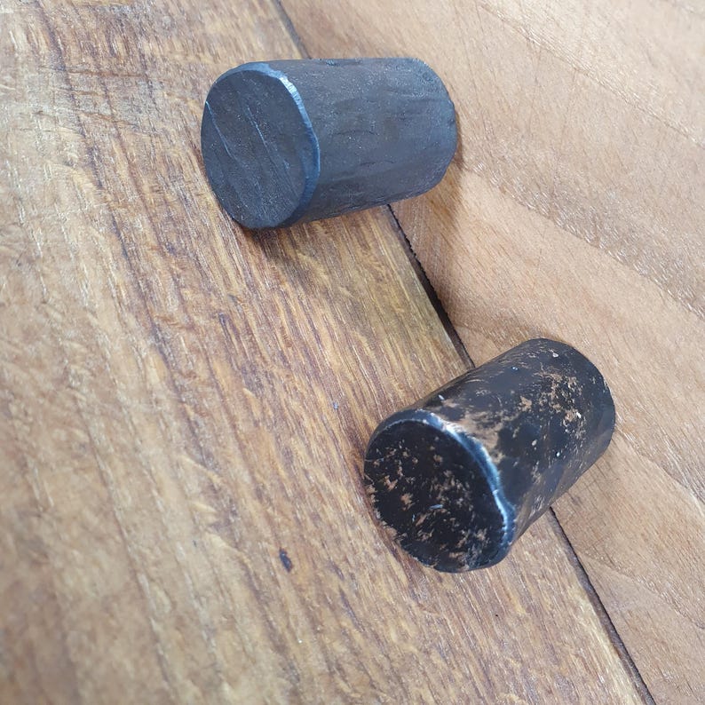 May include: Two black metal drawer pulls with a cylindrical shape. The pull on the left is smooth and the pull on the right has a textured finish.