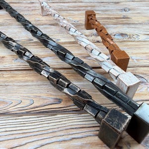 Könnte beinhalten: Drei Schrankgriffe aus Metall mit gedrehtem, seilartigem Design. Ein Griff ist dunkel anthrazit mit abgenutztem Finish, einer ist weiß mit verwitterter Textur und einer ist kupferbraun. Jeder Griff verfügt über quadratische Befestigungsblöcke.