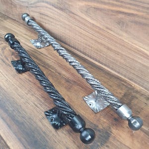 May include: Two twisted metal door pulls, one black and one silver, with decorative end caps and square mounting plates.