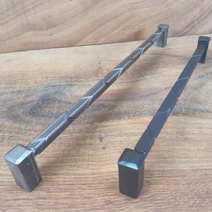 May include: Two black metal drawer pulls with a geometric design. The pulls are about 12 inches long and have a square shape at the ends.