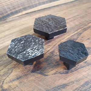 Puede incluir: Tres pomos hexagonales negros para armario con acabado texturizado. Los pomos son de diferentes tamaños.