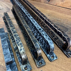 May include: Four elongated metal door handles with a hammered, textured surface. The handles feature varying metallic finishes, including dark bronze, silver, and gold tones, each with mounting plates at both ends containing screw holes.