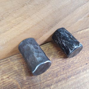 Può includere: Due tiretti per cassetti in metallo nero con finitura martellata. I tiretti sono di forma cilindrica e hanno un bordo leggermente arrotondato.