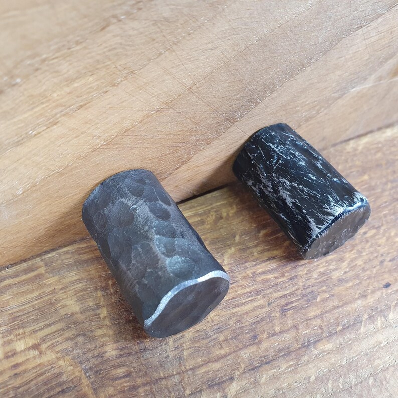 May include: Two black metal drawer pulls with a hammered finish. The pulls are cylindrical in shape and have a slightly rounded edge.