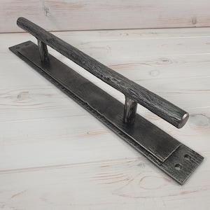 May include: A long, black metal door handle with a textured finish. The handle is mounted on a rectangular metal plate.