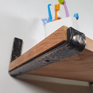 Peut inclure: Étagère flottante en bois avec des supports en métal foncé. L'étagère est en bois brun clair avec une garniture et des supports en métal foncé. Un récipient blanc avec des brosses à dents est posé sur l'étagère.