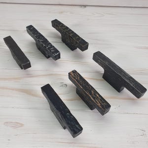 Könnte beinhalten: Sechs schwarze Metall-Schrankgriffe mit gehämmerter Oberfläche. Die Griffe sind in verschiedenen Größen und Formen, einige haben eine leicht abgenutzte Optik.