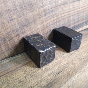 May include: Two black wooden blocks with a rough, textured surface. The blocks are rectangular in shape and have a slightly worn appearance.