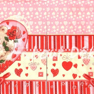 May include: A decorative paper napkin with a Valentine's Day theme. The design features a teddy bear holding a red rose inside a heart, surrounded by hearts and ribbons in shades of pink and red.