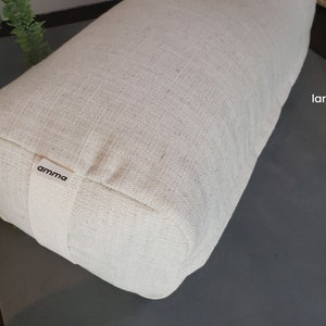 May include: A large, off-white, rectangular meditation cushion with a "amma" label. The cushion is made of a natural fabric and is sitting on a gray surface.
