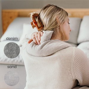 Peut inclure: Une femme portant un pull blanc est assise sur un canapé. Deux échantillons de tissu sont affichés en dessous d'elle, étiquetés "denim" et "sable".