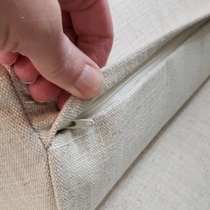 May include: A close-up of a zipper on a beige fabric cushion. The zipper is partially open, revealing the inside of the cushion.