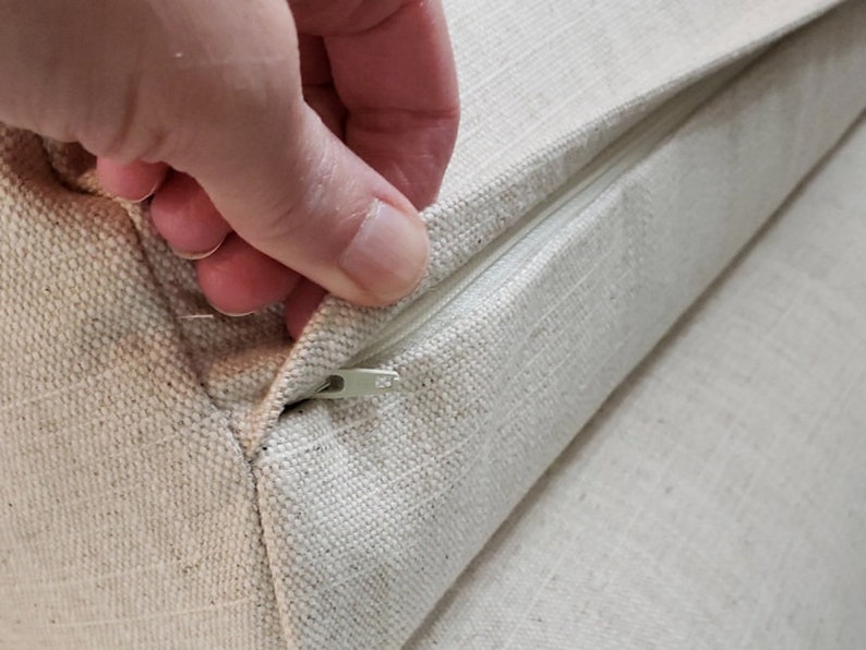 May include: A close-up of a zipper on a beige fabric cushion. The zipper is partially open, revealing the inside of the cushion.