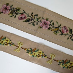 May include: Two beige needlepoint panels with floral and bird designs. The top panel features pink flowers, green leaves, and yellow birds. The bottom panel features yellow flowers, green leaves, and a brown ribbon.