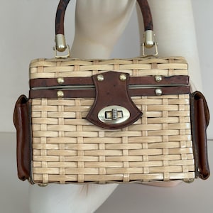 Könnte beinhalten: Vintage rechteckige Handtasche mit gewebtem Strohkörper und dunkelbraunen Lederakzenten. Die Tasche verfügt über einen oberen Griff, einen Schnallenverschluss und kleine Seitentaschen. Goldfarbene Hardware verleiht diesem klassischen Accessoire einen Hauch von Eleganz.