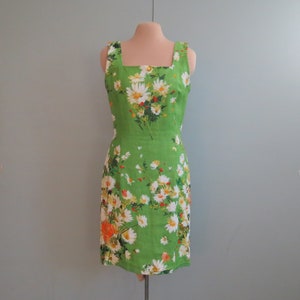 May include: A sleeveless green dress with a square neckline and a floral print featuring white daisies, red berries, and orange flowers.