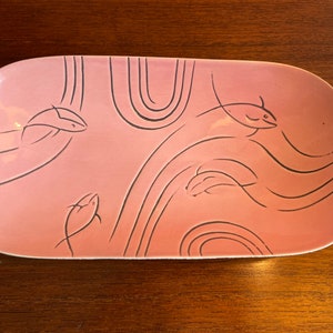May include: A pink oval ceramic serving dish with a black stylized design of fish swimming in waves.