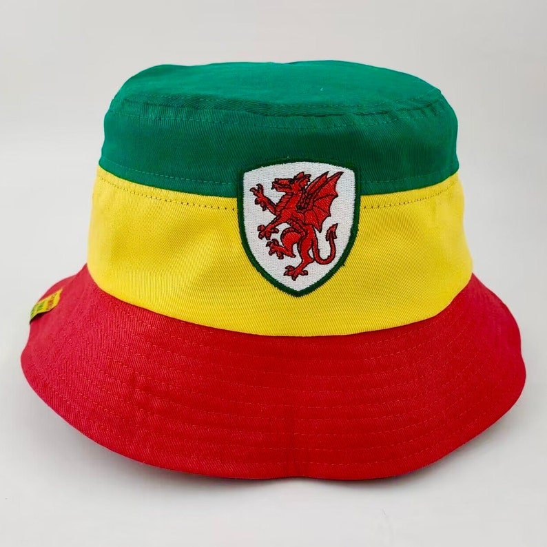 May include: A green, yellow, and red bucket hat with a red dragon emblem on the front. The dragon is on a white shield with a green border.