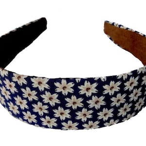 May include: A navy blue headband with a white floral pattern. The headband is made of fabric and has a brown suede backing.