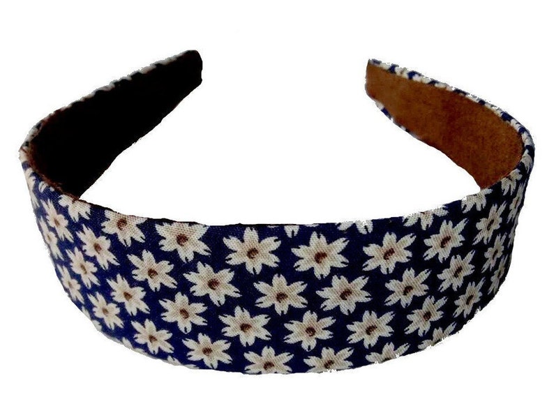 May include: A navy blue headband with a white floral pattern. The headband is made of fabric and has a brown suede backing.