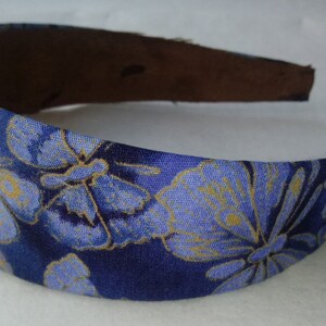 May include: A blue headband with a floral pattern in shades of blue and gold. The headband's interior is a dark brown color. This accessory is suitable for various occasions and adds a touch of elegance.