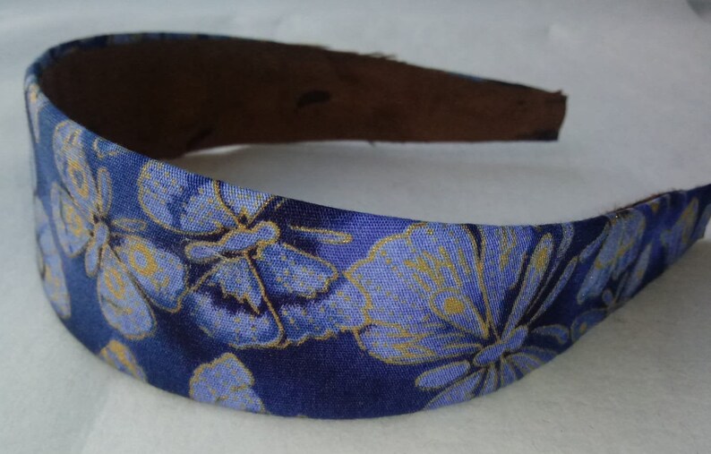 May include: A blue headband with a floral pattern in shades of blue and gold. The headband's interior is a dark brown color. This accessory is suitable for various occasions and adds a touch of elegance.