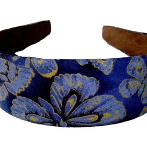 May include: A blue headband with a floral pattern in light blue and gold. The interior of the headband is a brown, suede-like material. This accessory is suitable for various hairstyles.