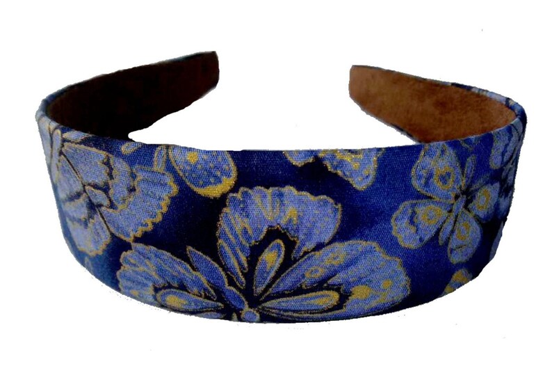 May include: A blue headband with a floral pattern in light blue and gold. The interior of the headband is a brown, suede-like material. This accessory is suitable for various hairstyles.