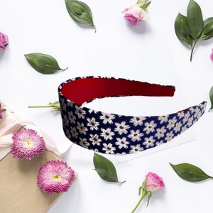 May include: A navy blue headband with a white floral pattern. The headband has a red lining and is surrounded by pink roses and green leaves.
