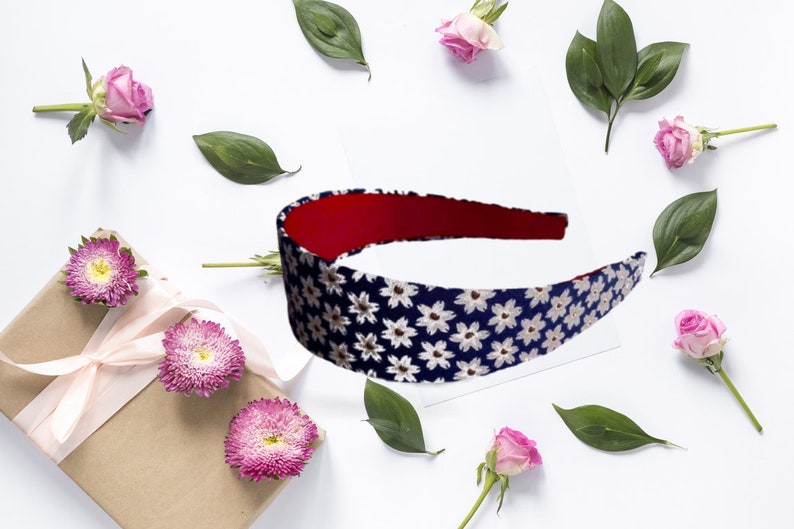 May include: A navy blue headband with a white floral pattern. The headband has a red lining and is surrounded by pink roses and green leaves.