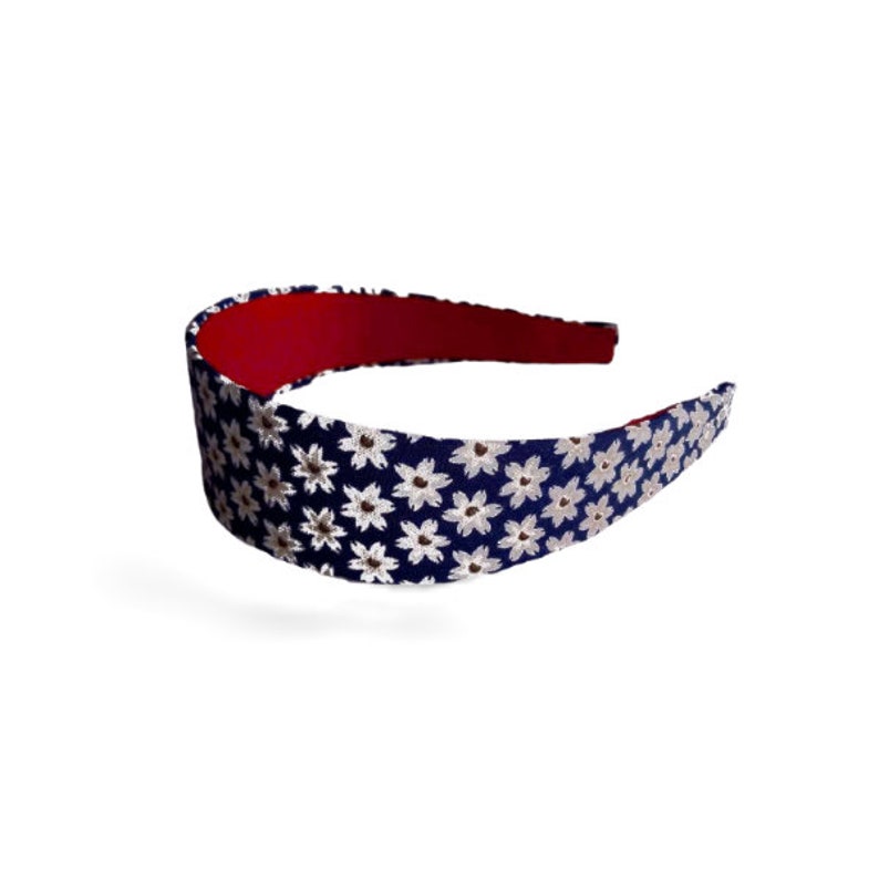 May include: A navy blue headband with a white floral pattern. The headband has a red lining.