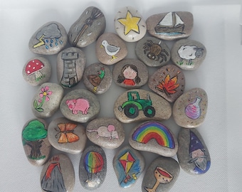 Può includere: Una collezione di sassi dipinti a mano con varie illustrazioni colorate. I disegni includono una stella, una barca a vela, una pecora, un fungo, una torre, una ragazza, un trattore, un arcobaleno e un mago. Ogni sasso è unico.