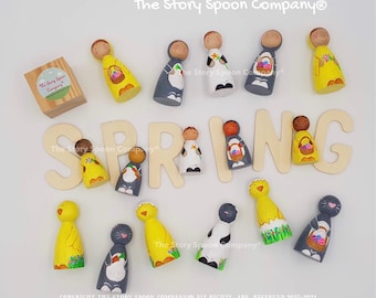 May include: A collection of hand-painted wooden peg dolls with spring-themed designs, including chicks, bunnies, and figures holding Easter baskets. The word "SPRING" is spelled out in wooden letters. The Story Spoon Company logo is visible.