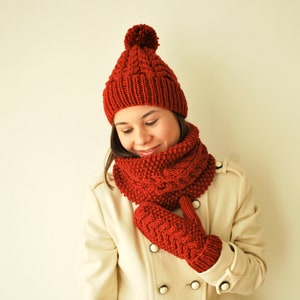 Könnte beinhalten: Eine rote Strickmütze mit Bommel, ein passender roter Strickschal und rote Strickhandschuhe.