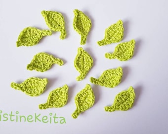May include: A collection of 12 crocheted green leaves, arranged in a circular pattern on a white background. The leaves are all the same size and shape, and they have a slightly textured surface.