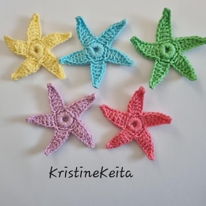 Peut inclure: Cinq étoiles de mer crochetées en jaune, bleu clair, vert, lavande et corail. Chaque étoile de mer présente une ouverture circulaire centrale et cinq bras pointus. Le texte KristineKeita est imprimé en noir sous les étoiles.