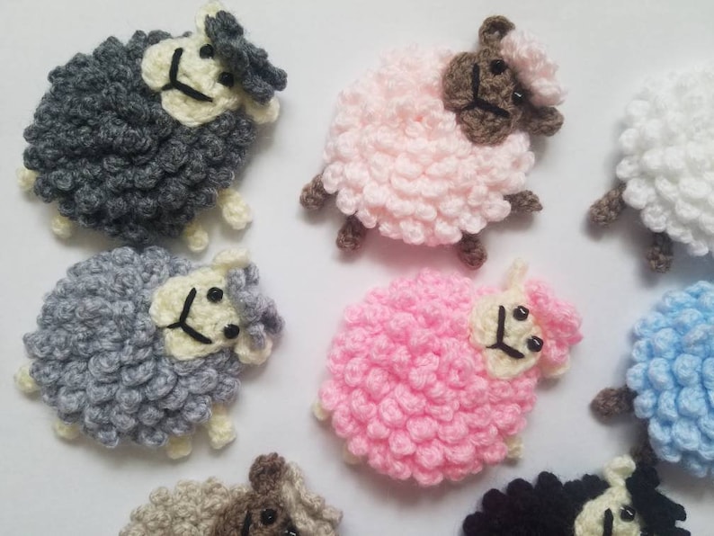 May include: A collection of ten crocheted sheep in various colors, including pink, gray, white, and blue. Each sheep has a white face with black eyes and a black nose.