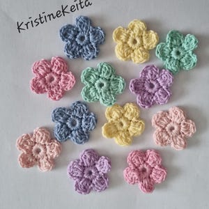 May include: A collection of twelve small, five-petaled crochet flowers in pastel shades of blue, yellow, mint green, pink, and lavender. The text "Kristinekeita" is printed in black in the upper left corner of the image.