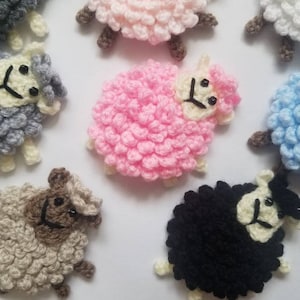 May include: A collection of crocheted sheep in various colors, including pink, blue, gray, white, and black. Each sheep has a fluffy, textured body and a cute face with black eyes and a smile.
