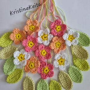 Puede incluir: Una colección de flores y hojas de ganchillo en tonos melocotón, rosa, blanco y verde claro, todas unidas a hilos individuales que se reúnen en la parte superior. El texto Kristinekeita está impreso en negro en la parte superior izquierda.