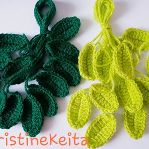 May include: Two clusters of crocheted leaves, one in dark green and the other in lime green. The leaves are attached to yarn stems. The text "KristineKeita" is visible at the bottom of the image.