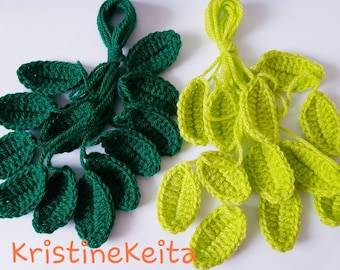 May include: Crocheted leaf clusters in two shades of green. One cluster is a deep forest green, the other is a bright lime green. The leaves are connected by yarn stems. The text "KristineKeita" is visible at the bottom.