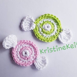 May include: Two crocheted candy shapes, one pink and white, the other green and white, with white crocheted loops on each side. The text "KristineKeita" is visible in the background.
