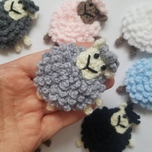 May include: A collection of crocheted sheep in various colors, including gray, white, pink, blue, and black. The sheep are all small and have a fluffy texture.