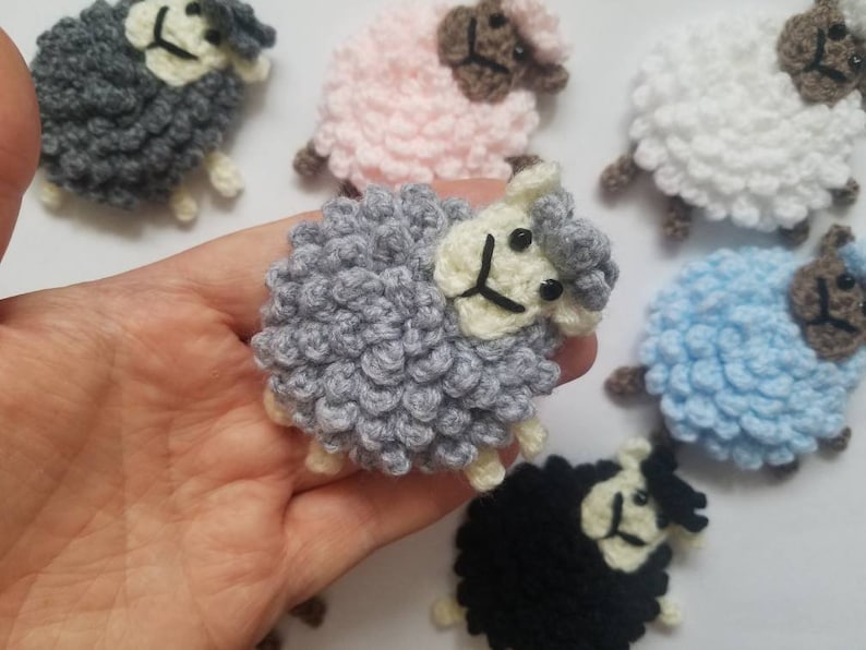 May include: A collection of crocheted sheep in various colors, including gray, white, pink, blue, and black. The sheep are all small and have a fluffy texture.