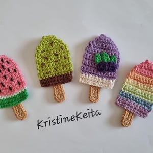 Puede incluir: Cuatro diseños de paletas de crochet coloridas. Una tiene temática de sandía, otra es verde, una tercera es morada con detalles de bayas y la última es de arcoíris. Cada una tiene un palito de madera. El texto "Kristinekeita" está escrito en cursiva negra.