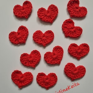 May include: A collection of eleven handmade red crochet hearts. The hearts are arranged on a white surface. The text "Kristinekeita" is written in red script in the bottom right corner.