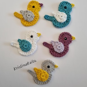 May include: Five crocheted bird appliques in various colour combinations including yellow with grey, blue with white, white with teal, purple with light purple, and grey with yellow. Each bird features a small black eye and a yellow beak. Text reads KristineKeita.
