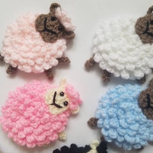 May include: A collection of crocheted sheep in pink, white, and blue. Each sheep has a brown face and a fluffy body.