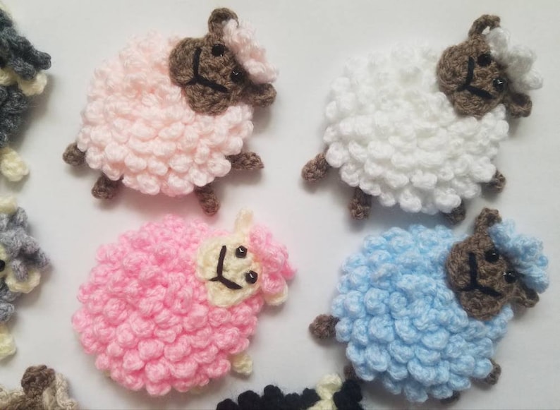 May include: A collection of crocheted sheep in pink, white, and blue. Each sheep has a brown face and a fluffy body.